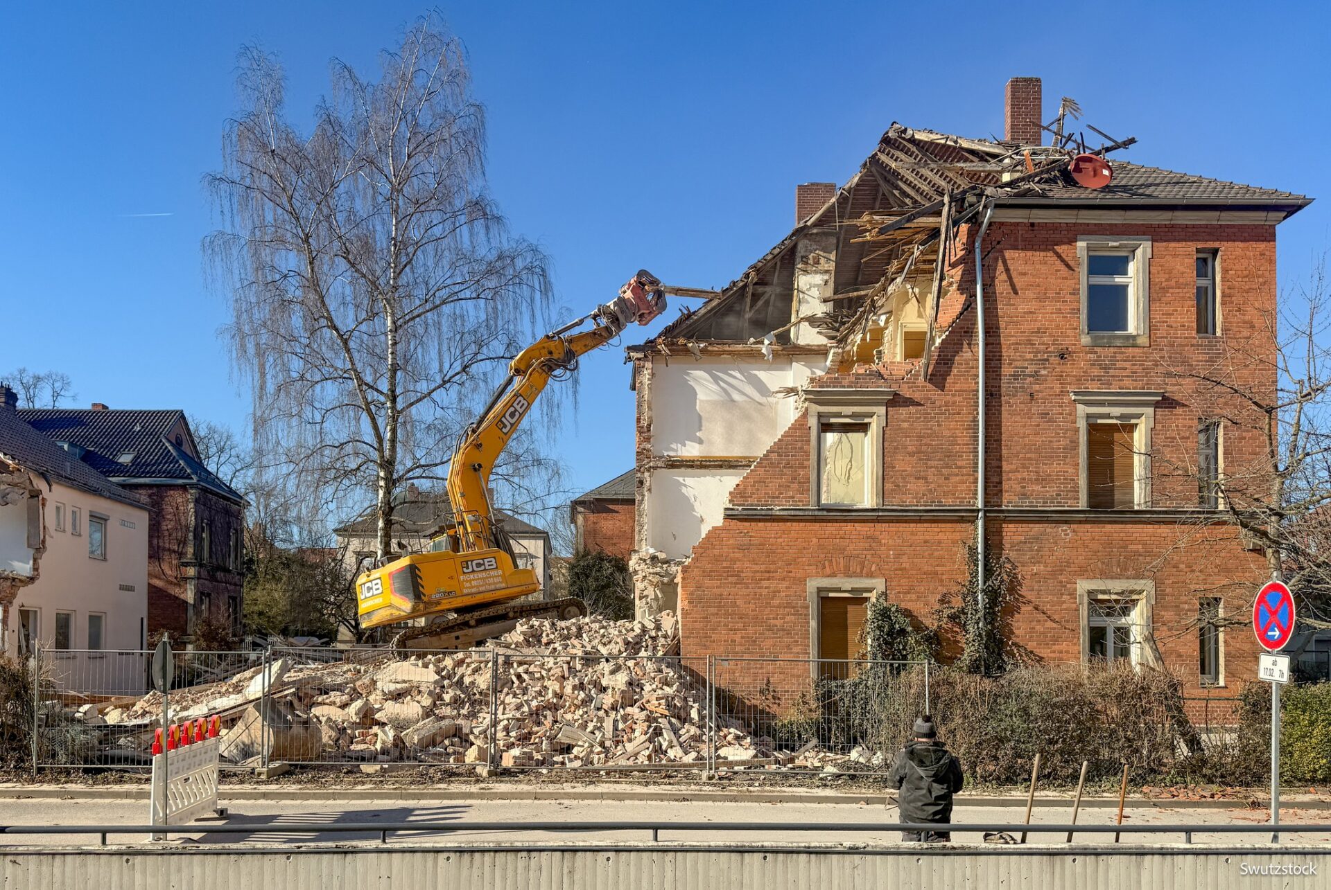 Ein Bagger bricht ein altes drestöckiges Haus aus Backstien ab.