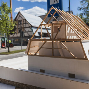Ein Modell eines Fachwerkhauses im Vordergrund, im Hintergrund ist das gleiche Haus tatsächlich gebaut zu sehen, dazwischen eine Straße.