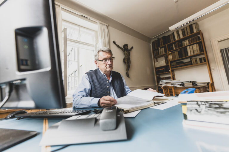 Michael Ritter sitzt an einem Schreibtsich und liest in einem Buch.