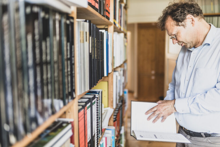 Vinzenz Dufter vor einem Bücherregal, er hält ein Buch in der Hand.