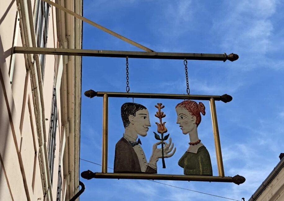 Wirtshausschild in Ungarn mit einem Mann, der einer Frau eine Blume überreicht