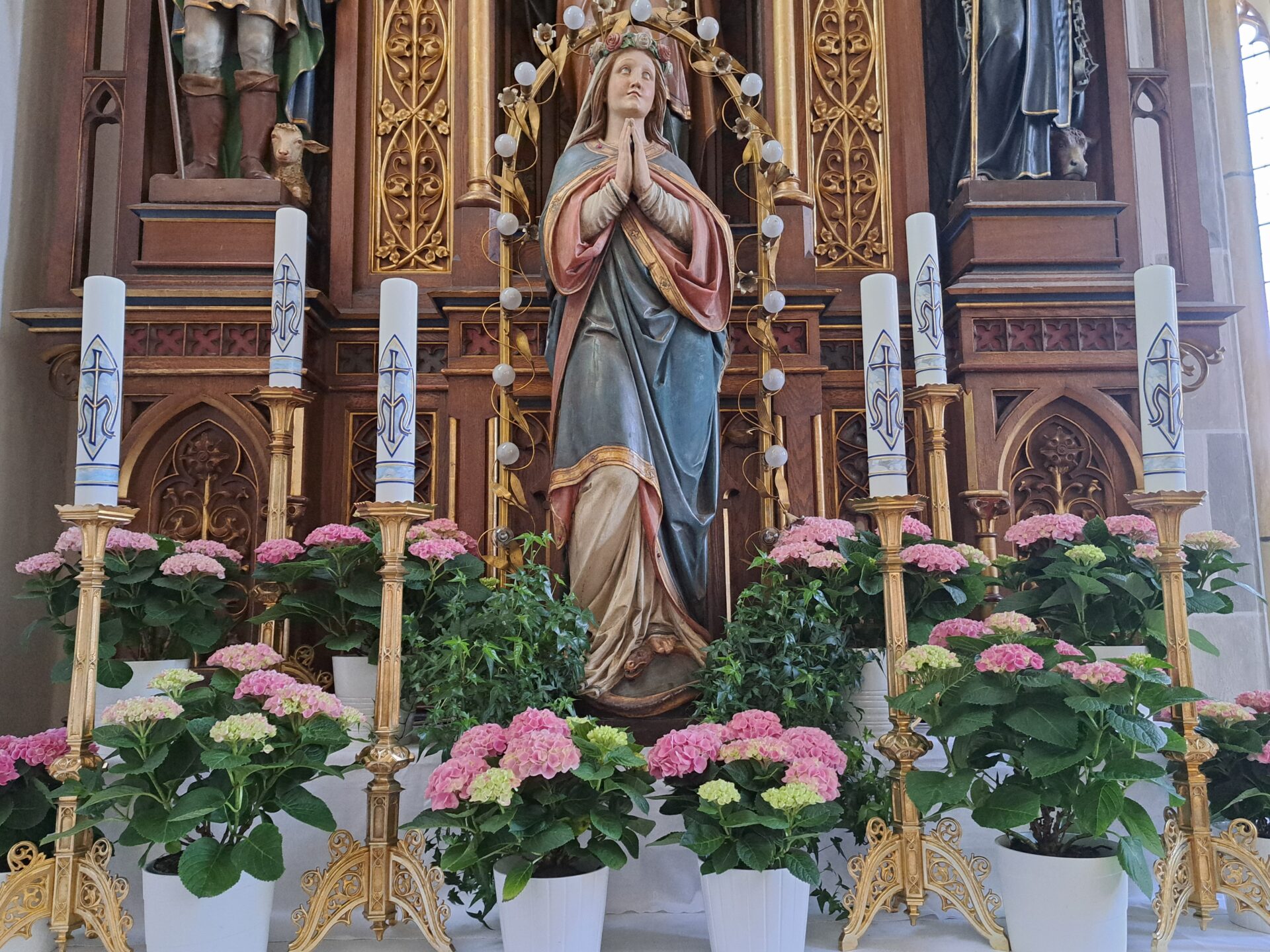 Marienstatue umgeben mit Kerzen und Blumen